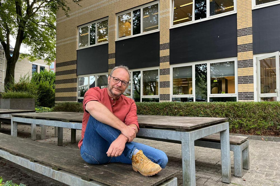 Hans Dehing op een bankje voor een schoolgebouw.