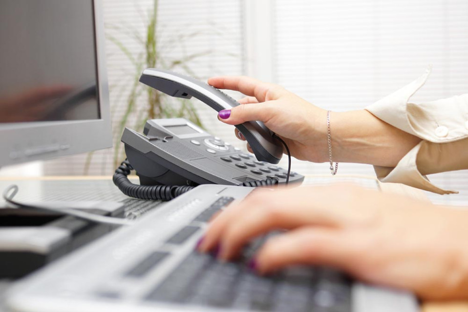 Je ziet een hand op een toetsenbord en de andere hand neemt telefoon op.