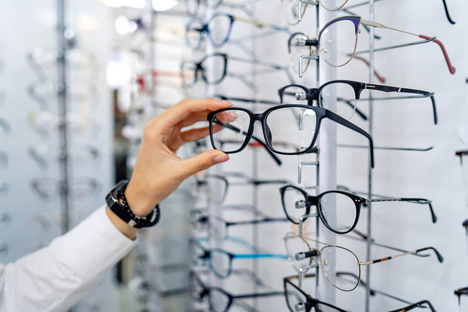 Hand pakt bril uit wand bij optiekwinkel.