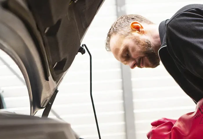 Monteur werkt aan electrische auto. Hij heeft isolerende handschoenen aan.