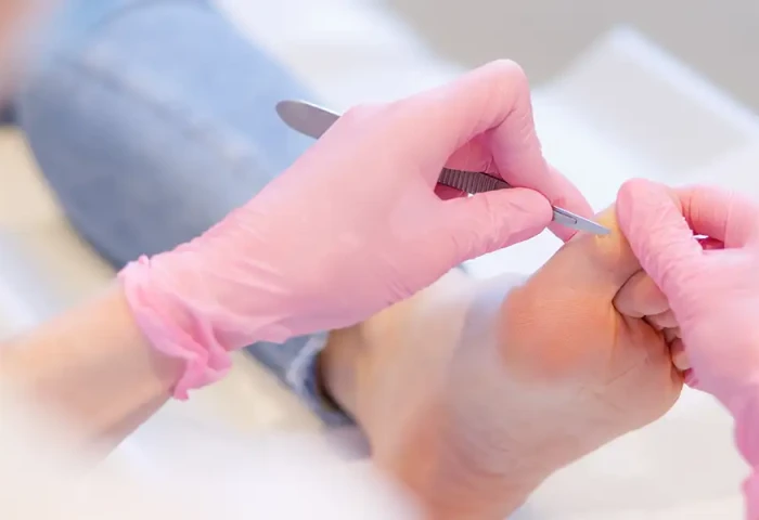 Handen van pedicure in latex handschoenen werken aan een voet van een client.