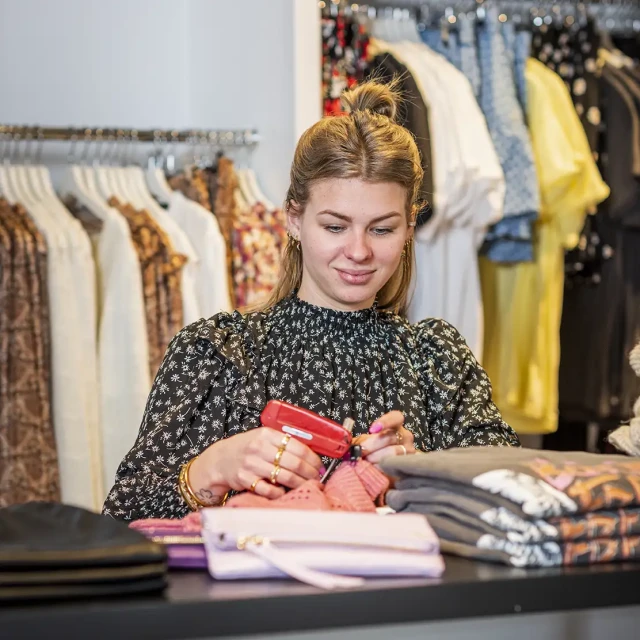 Verkoopster van kleding prijst artikelen achter de toonbank