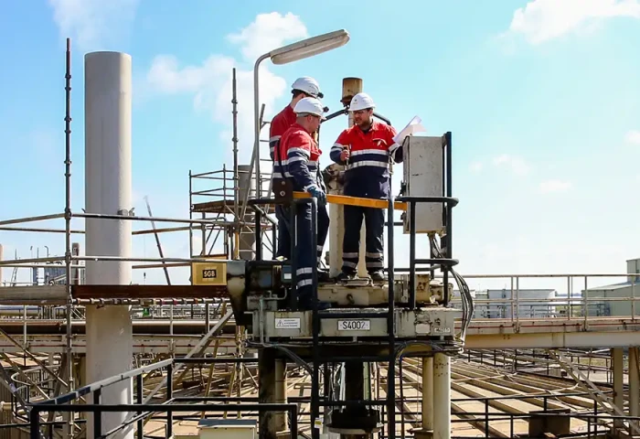 Vakmensen staan op een platform boven de fabriek. Ze zijn aan het overleggen.