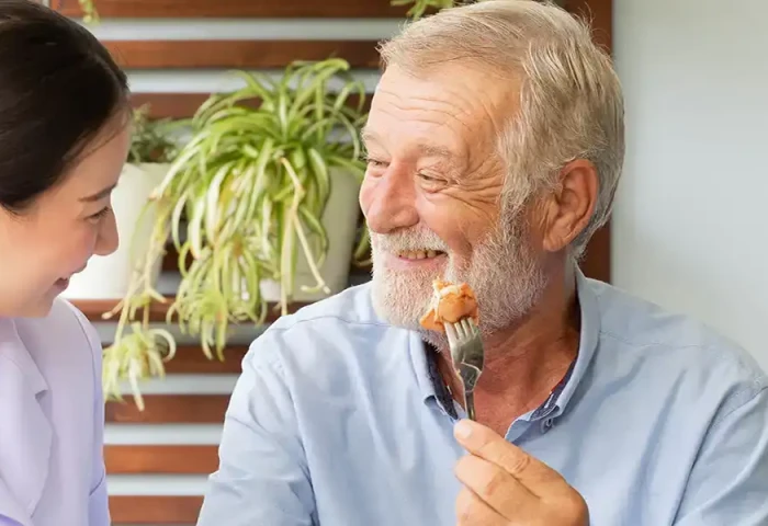 Oudere man en helpende. De man houdt een vork met een kipnugget omhoog.