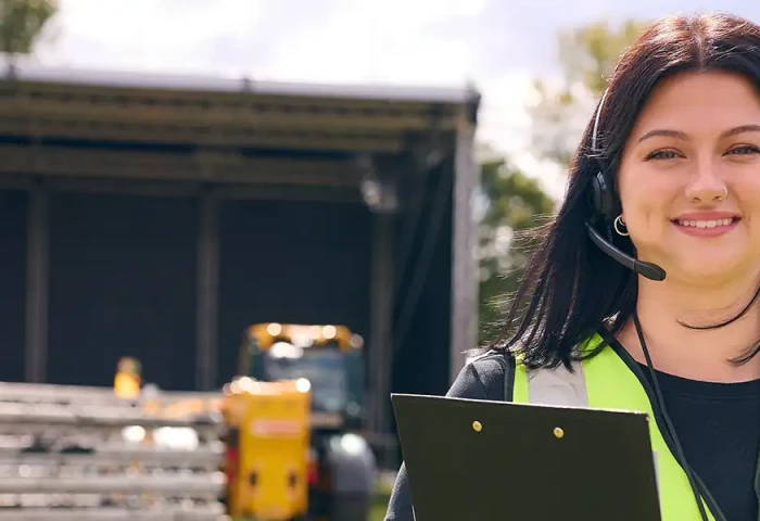 Vrouw met veiligheidshes en klembord poseert voor een podium
