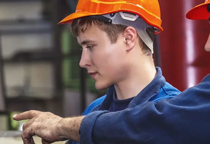 Oudere werknemer in de productie laat iets zien aan een junior op een smartphone.