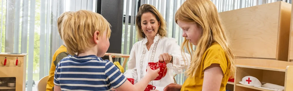 Kleuterleidster drinkt imaginaire thee met kinderen aan een tafeltje.