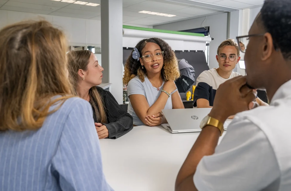 Groep studenten aan tafel met laptops voor zich bespreken iets.