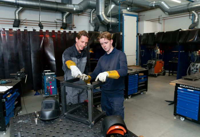 Instructeur en student samen in de werkplaats. De instructeur legt iets uit.